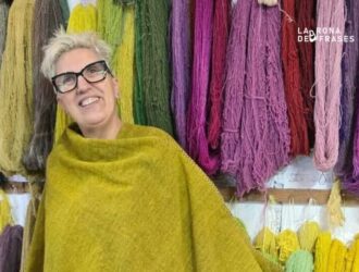 Ermi Fernández, artista de Tramas Convergentes, con un chal de lana frente a madejas teñidas con tintes naturales